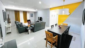 Ein modernes Wohnzimmer mit einer Couch, einem Esstisch mit Stühlen, einem Fernseher und einer gelben Akzentwand.