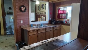A kitchen with wooden cabinets, a stove, a sink, and a window with a red curtain. - Our Guest house is a cozy get away, in a small town.  (Grey Eagle)