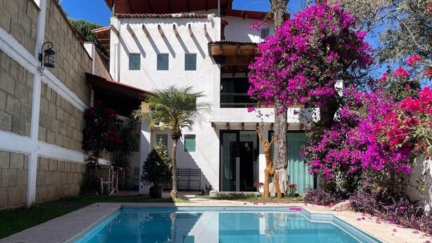 A swimming pool with a clear blue water surface, surrounded by a garden with pink bougainvillea flowers and a palm tree. - Casa Valle de Bravo la Peña  (Valle de Bravo)