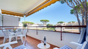 A balcony with white chairs, a round table, and a bottle of wine.