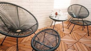 Een kamer met drie zwarte frame stoelen, een klein wit tafeltje met een decoratief object, en een houten vloer met een herringbone patroon.