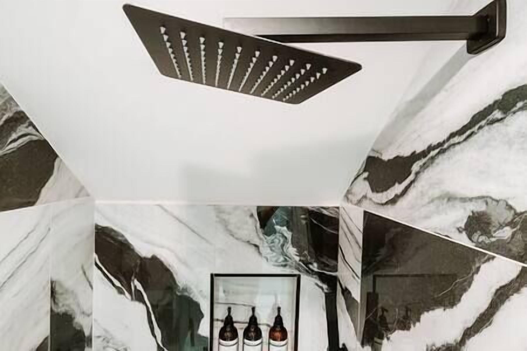 A bathroom with a shower head, marble walls, and three bottles on a shelf.
