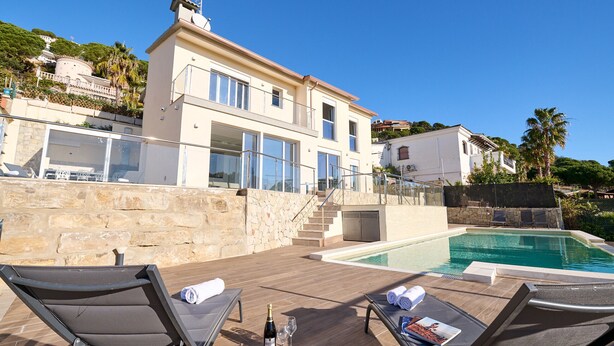 A modern villa with a swimming pool, outdoor seating, and a stone wall. - 2FIR02 Villa with private swimming pool (Lloret de Mar)