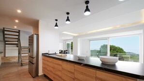 A modern kitchen with a wooden island, stainless steel appliances, and large windows offering a view of the outdoors. - 2FIR02 Villa with private swimming pool (Lloret de Mar)