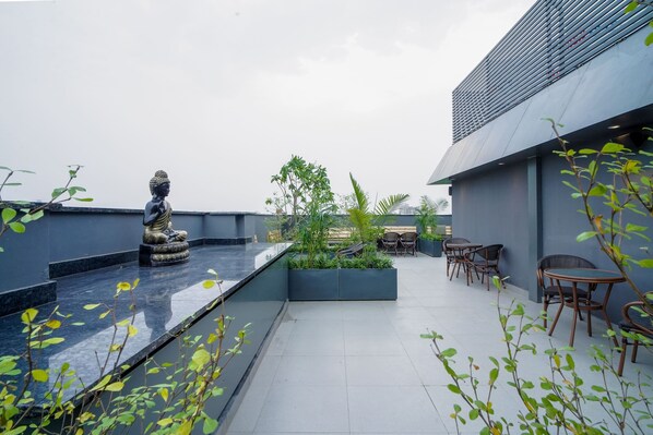 A rooftop terrace with a Buddha statue, seating area, and potted plants.