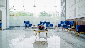 A modern lobby with a marble floor, blue upholstered chairs, and a central table with a floral arrangement. - Saltstayz Select - Golf Course Road & Sector 57 (Gurugram)