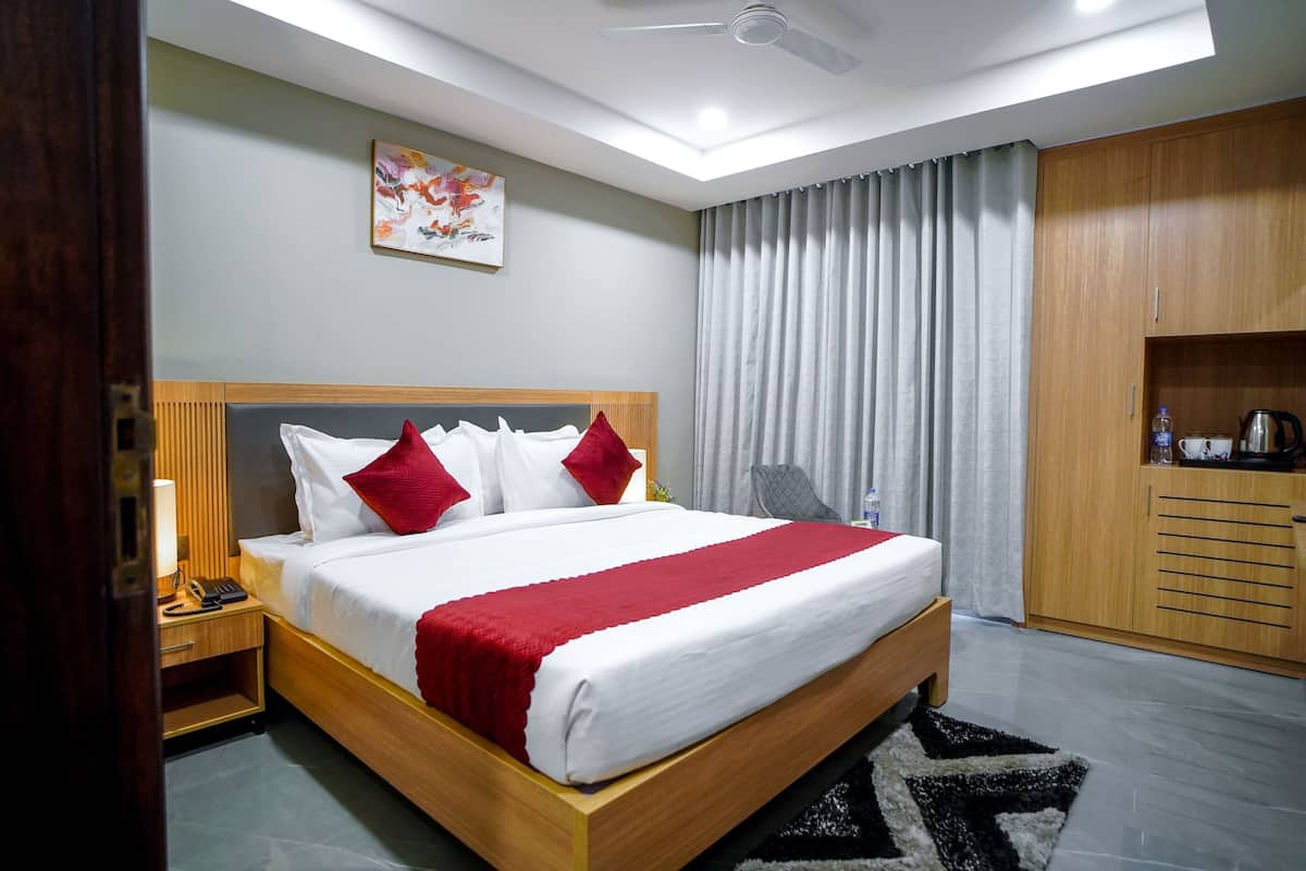 A hotel room with a wooden bed, a nightstand, a desk with a lamp, a wardrobe, and a ceiling fan.