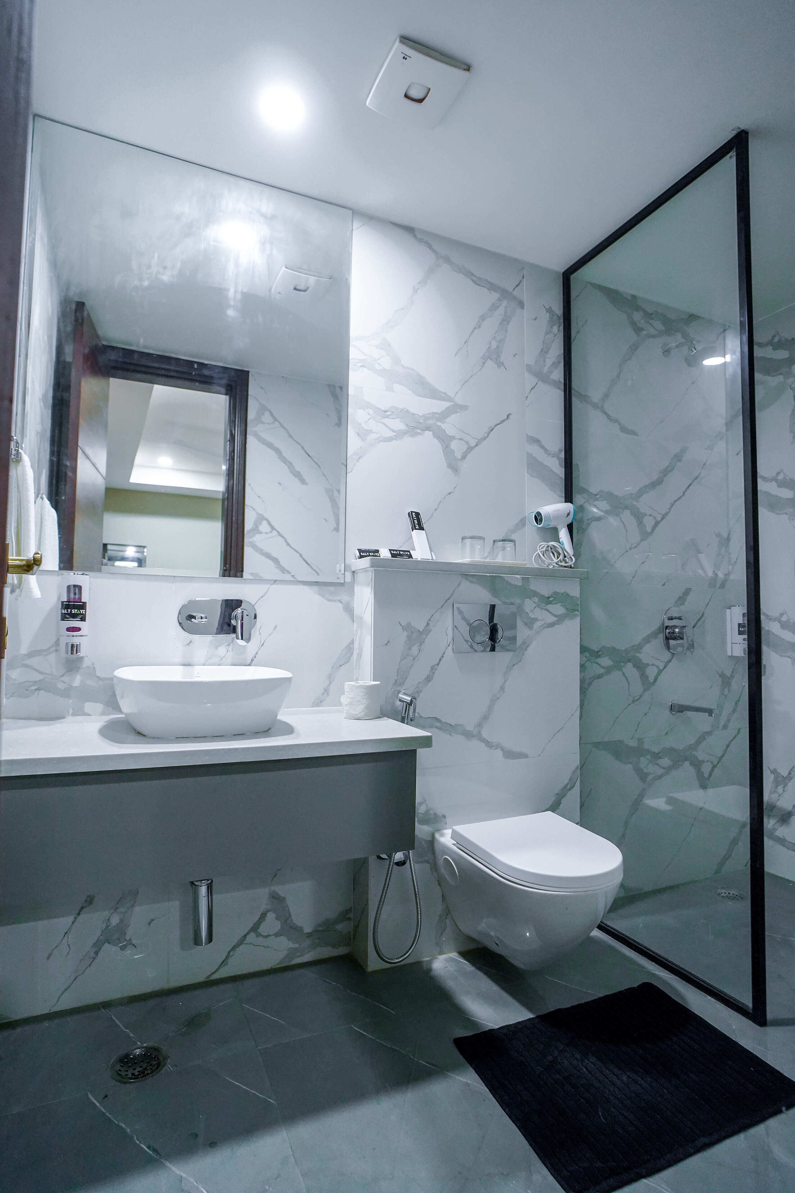 A modern bathroom with a marble backsplash, a white sink, a toilet, and a glass shower enclosure.