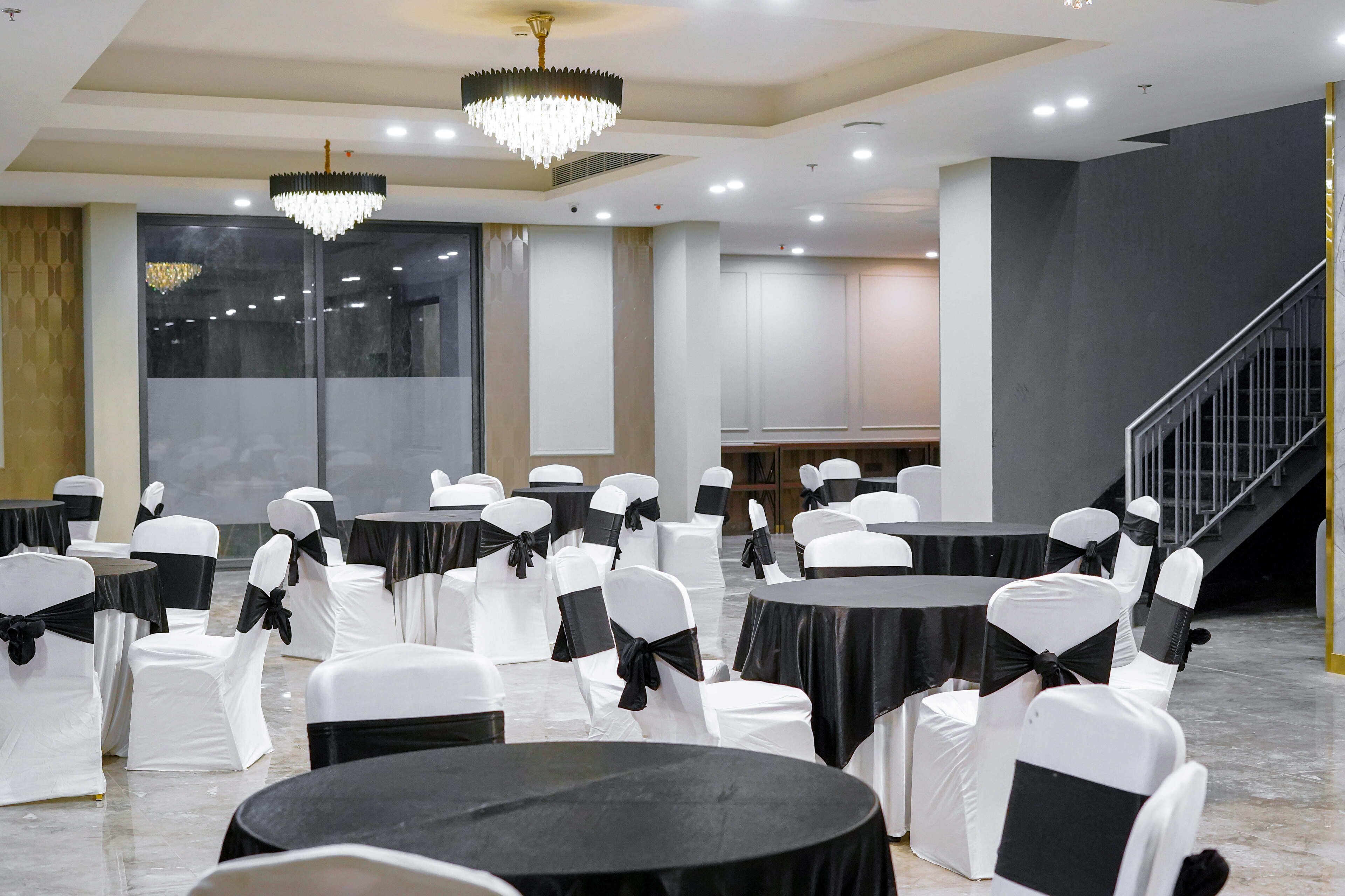 Un salón de conferencias con mesas redondas y sillas blancas, cintas negras y candelabros.