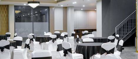 Un salón de conferencias con mesas redondas y sillas blancas, cintas negras y candelabros.