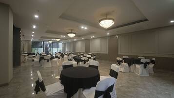 A spacious banquet hall with round tables, chairs with black sashes, and chandeliers.