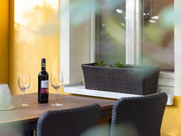 A table with a bottle of wine and two glasses, a wicker basket with plants, and a window with a view of greenery. - Apartment Pirol by Interhome (Zinnowitz)