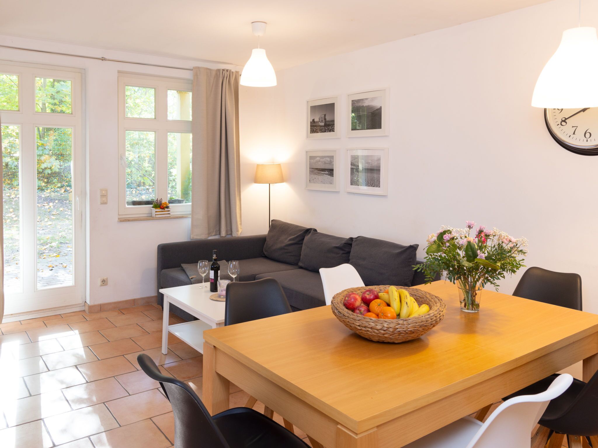 Una sala de estar moderna con un sofá, una mesa de comedor con sillas, un frutero, una lámpara y un reloj en la pared.