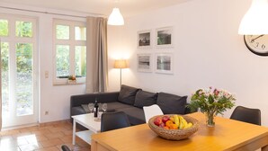 Moderni olohuone, jossa on sohva, ruokapöytä tuoleineen, hedelmäkulho, lamppu ja seinällä oleva kello.