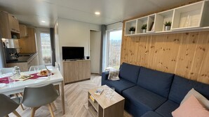 A modern living room with a sofa, a dining table with chairs, a TV, and a kitchen area.