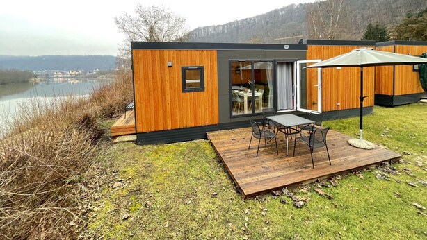 A modern cabin with a deck, a dining area, and a view of a lake and mountains.