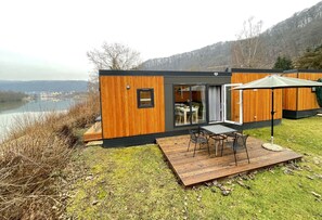 A modern cabin with a deck, a dining area, and a view of a lake and mountains. - Tiny Haus Schleusenblick by Interhome (Riedenburg)