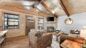 A cozy living room with wooden floors, a fireplace, a television, and a ceiling fan.