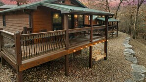 A wooden cabin with a deck, outdoor seating, and a stone pathway.