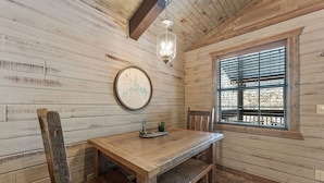 A rustic wooden interior with a wooden dining table, chairs, a map on the wall, and a window with blinds.