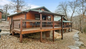 A wooden cabin with a porch, stone foundation, and a view of the surrounding forest.
