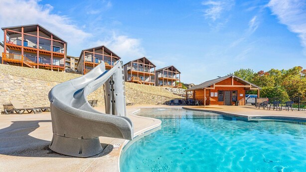 A swimming pool with a slide, stone walls, and wooden buildings with balconies.