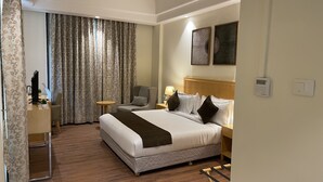 A hotel room with a large bed, a desk with a computer, a chair, a lamp, and a window with curtains. - Saltstayz Select - Galleria Market & Golf Course Road (Gurugram)