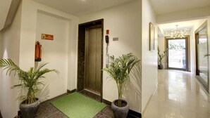 A hotel lobby with a fire exit sign, an elevator, and potted plants. - Saltstayz Select - Galleria Market & Golf Course Road (Gurugram)