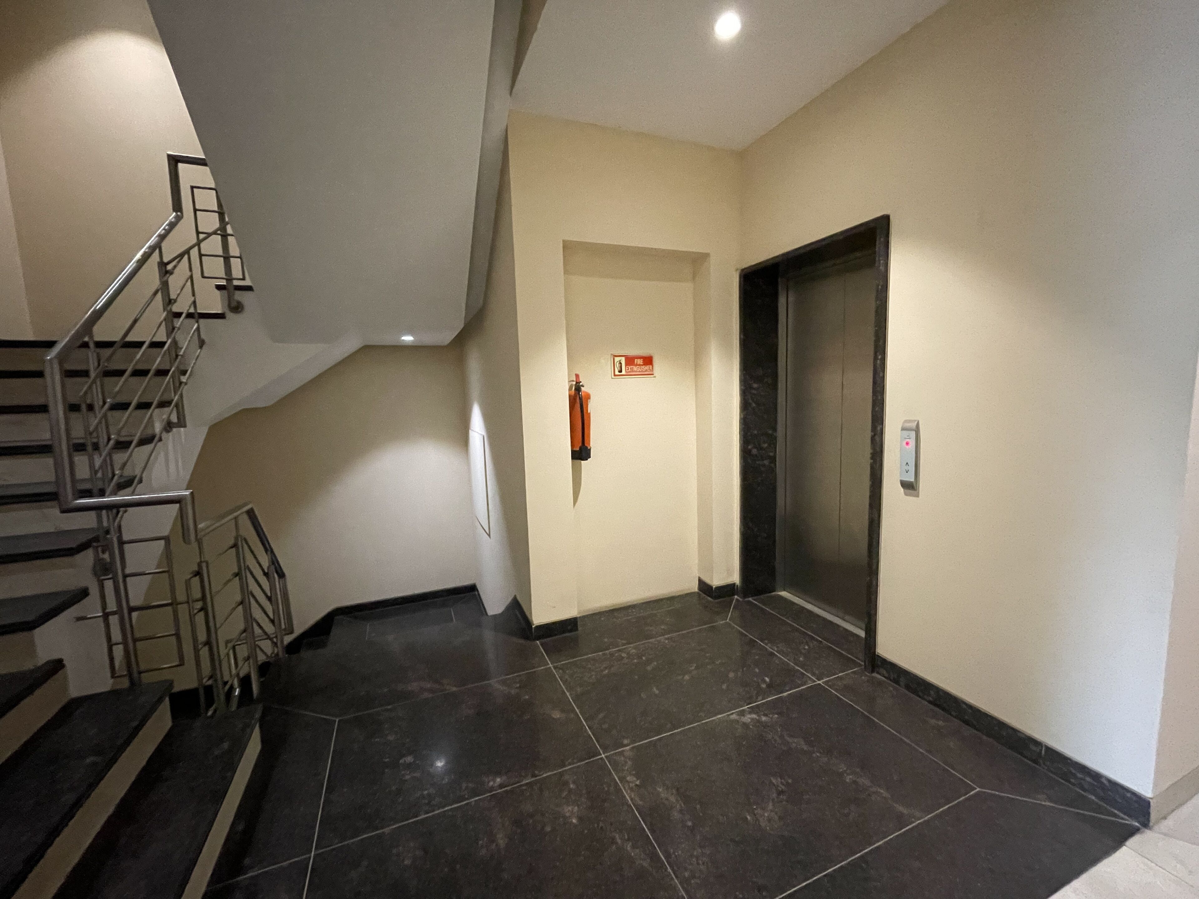 A hallway with a staircase, a fire extinguisher, and an elevator.