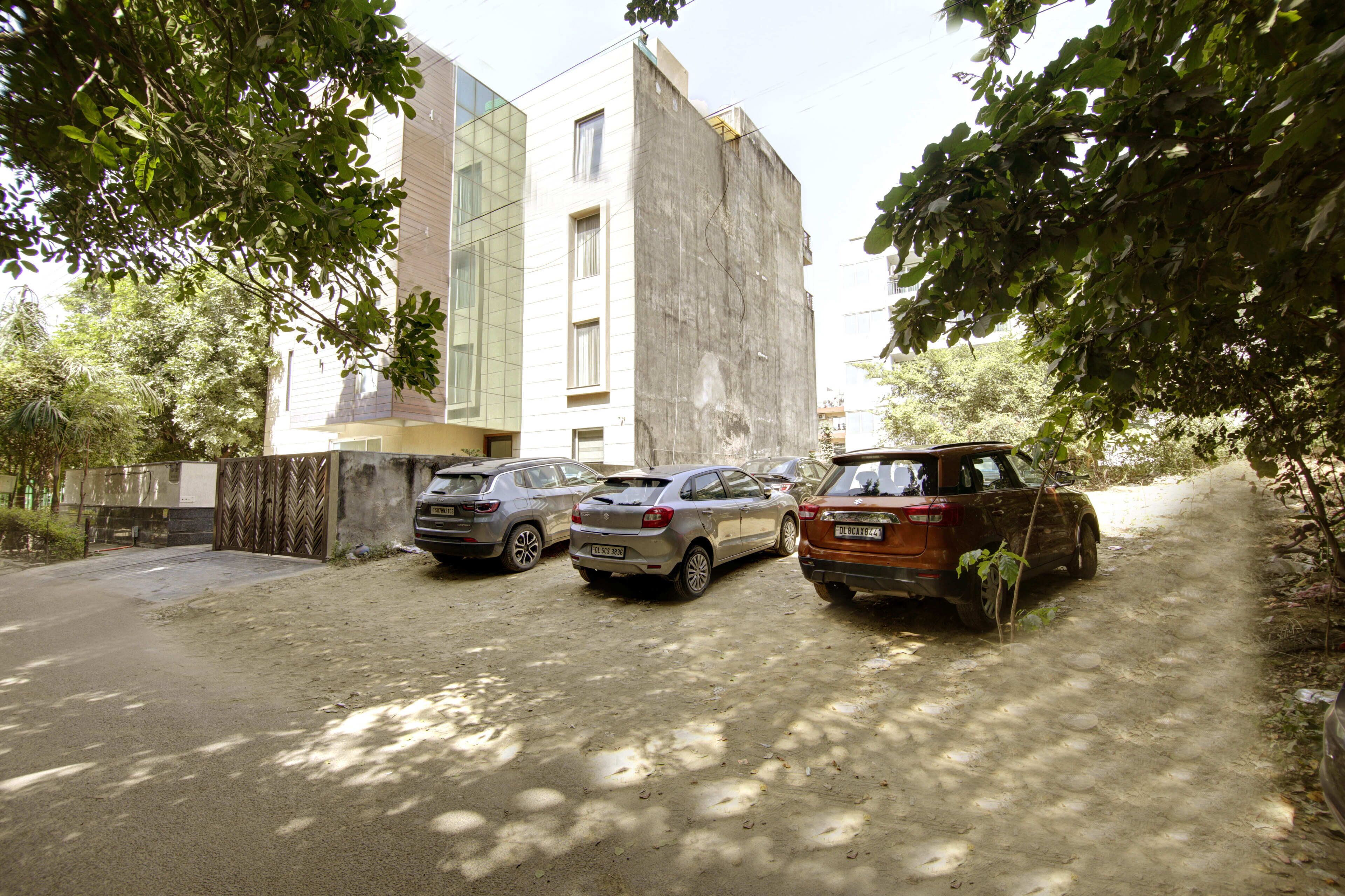 Un área de estacionamiento con tres coches aparcados frente a un edificio de diseño moderno, con fachada de vidrio y exterior de hormigón.