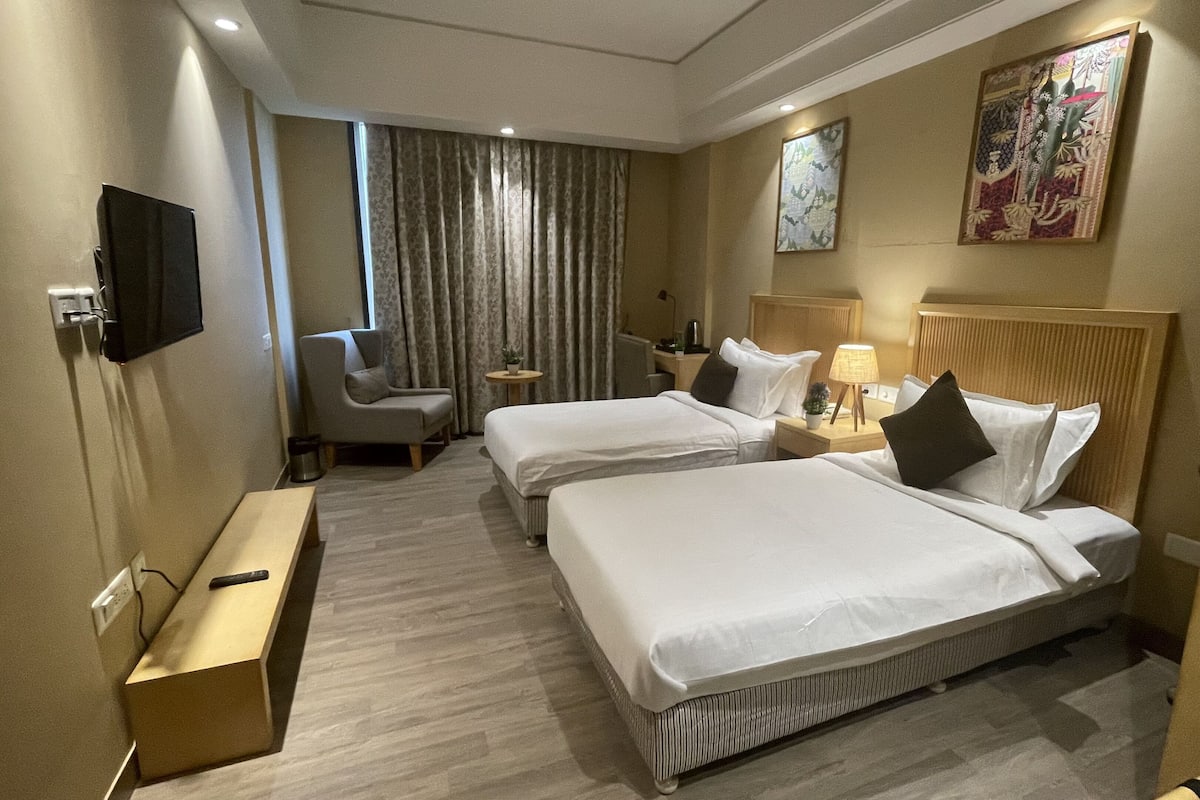 A hotel room with two beds, a desk, a chair, a TV, and a window with curtains.