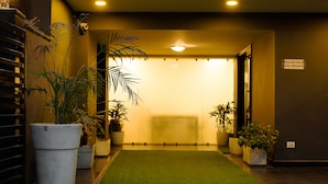 A hotel lobby with a green artificial turf leading to a reception area. There are potted plants on either side of the entrance. - Saltstayz Express - Golf Course Road & DLF Phase-1 (Gurugram)