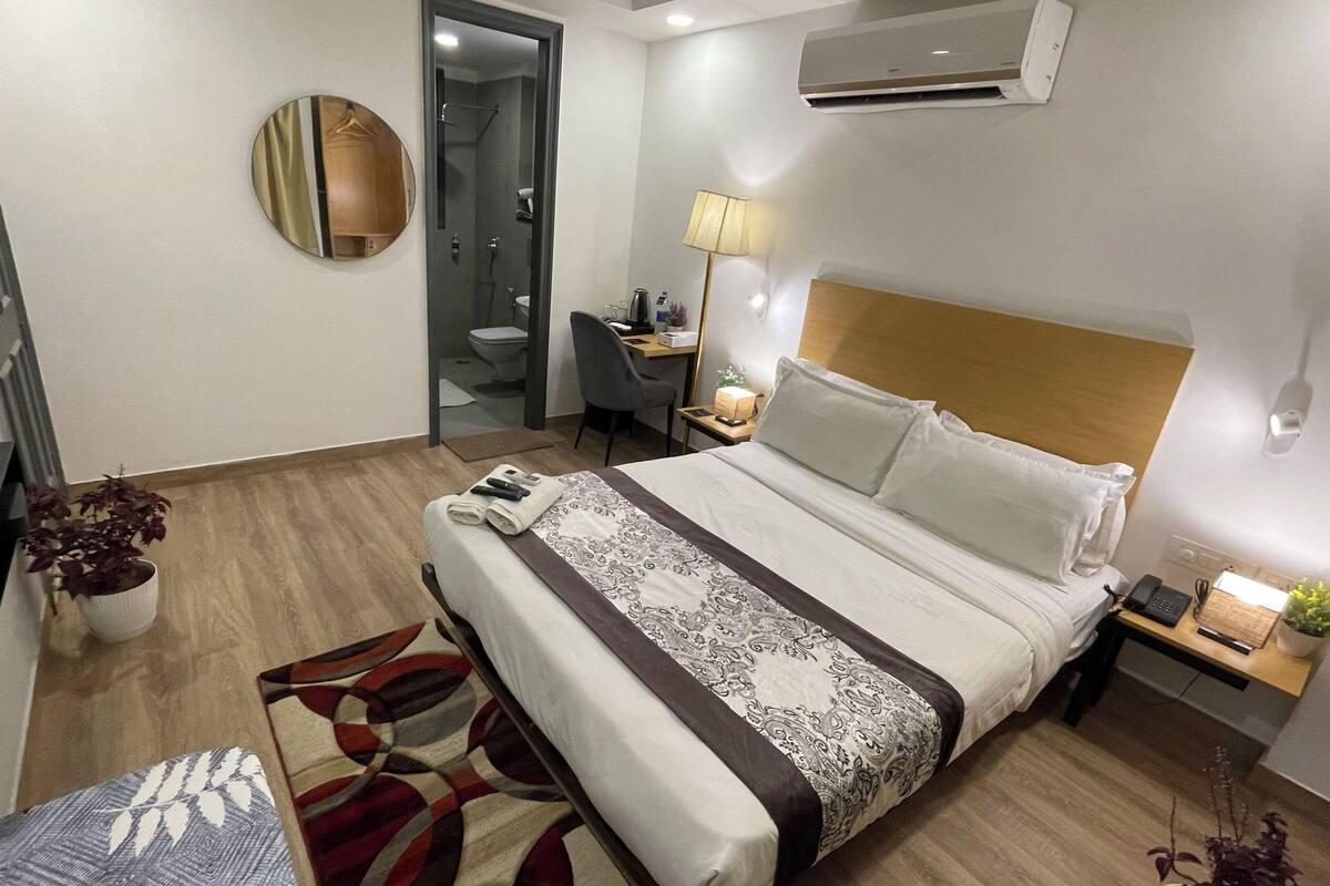 A hotel room with a bed, bedside table, lamp, and a desk with a chair.