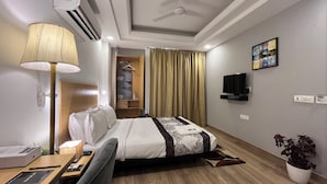 A hotel room with a bed, bedside table, lamp, TV, and a plant. - Saltstayz Express - Golf Course Road & DLF Phase-1 (Gurugram)