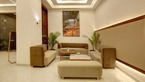 Un hall d’entrée moderne avec un canapé beige, deux fauteuils, une table basse et un grand tableau abstrait accroché au mur.