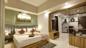 Une chambre moderne avec un grand lit, des tables de chevet, une petite table de nuit, une armoire en bois et un petit coin cuisine.