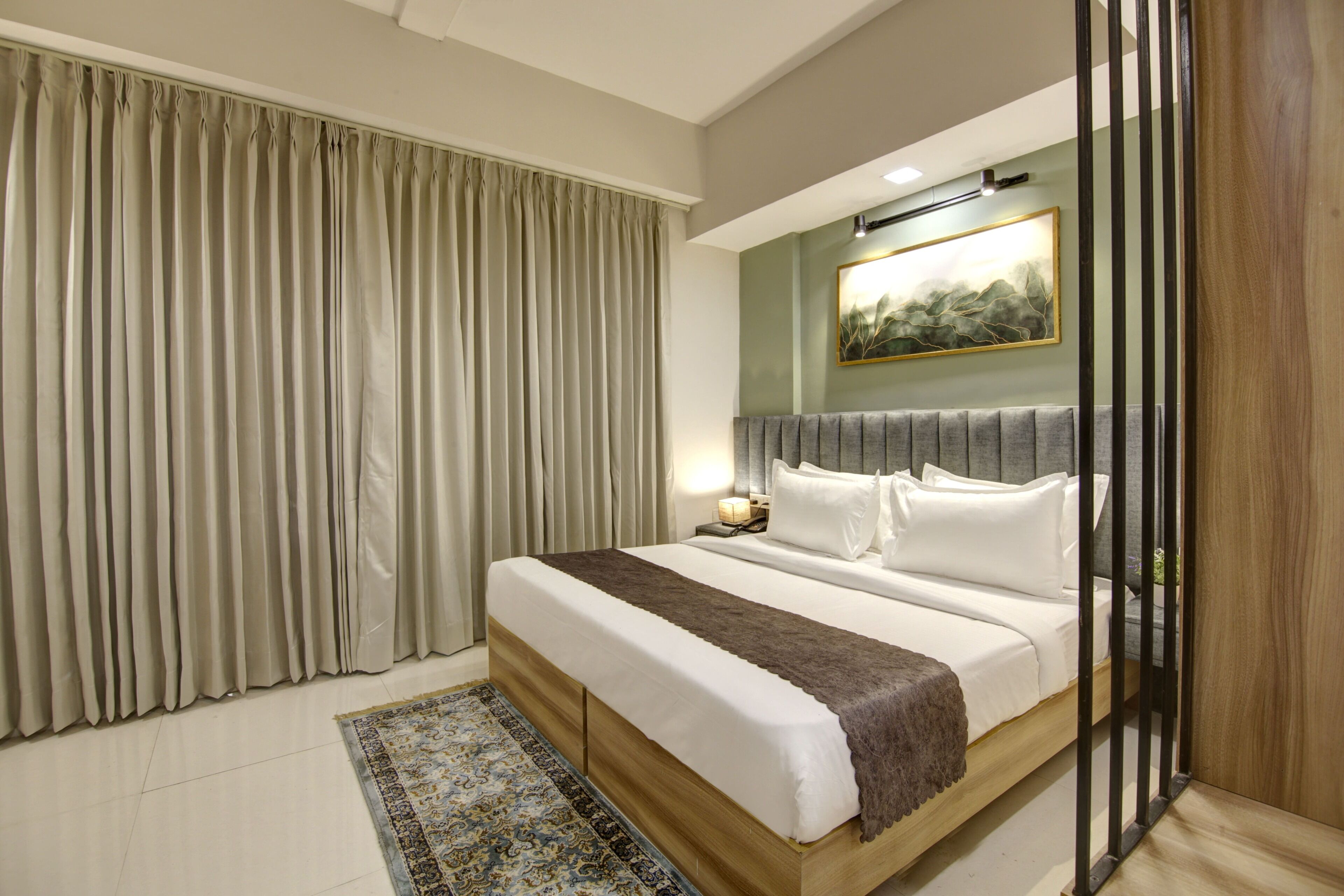 Una habitación de hotel moderna con una cama grande, una mesita de noche, una lámpara de pared y un cuadro sobre la cama.