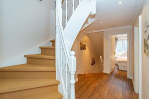 Un escalier avec des marches en bois et des balustrades blanches menant à une chambre à coucher où se trouvent un lit et une fenêtre.