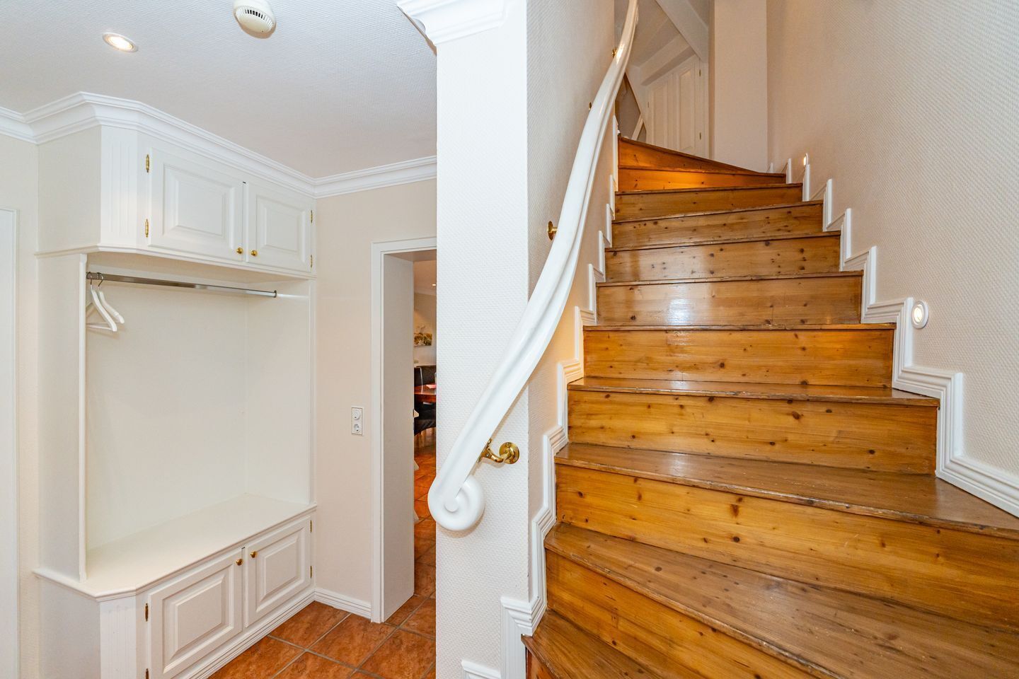 A wooden staircase with white railings and a white door with a gold handle.