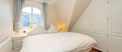 A bedroom with a large bed, a window with curtains, a nightstand with a lamp, and a wardrobe.