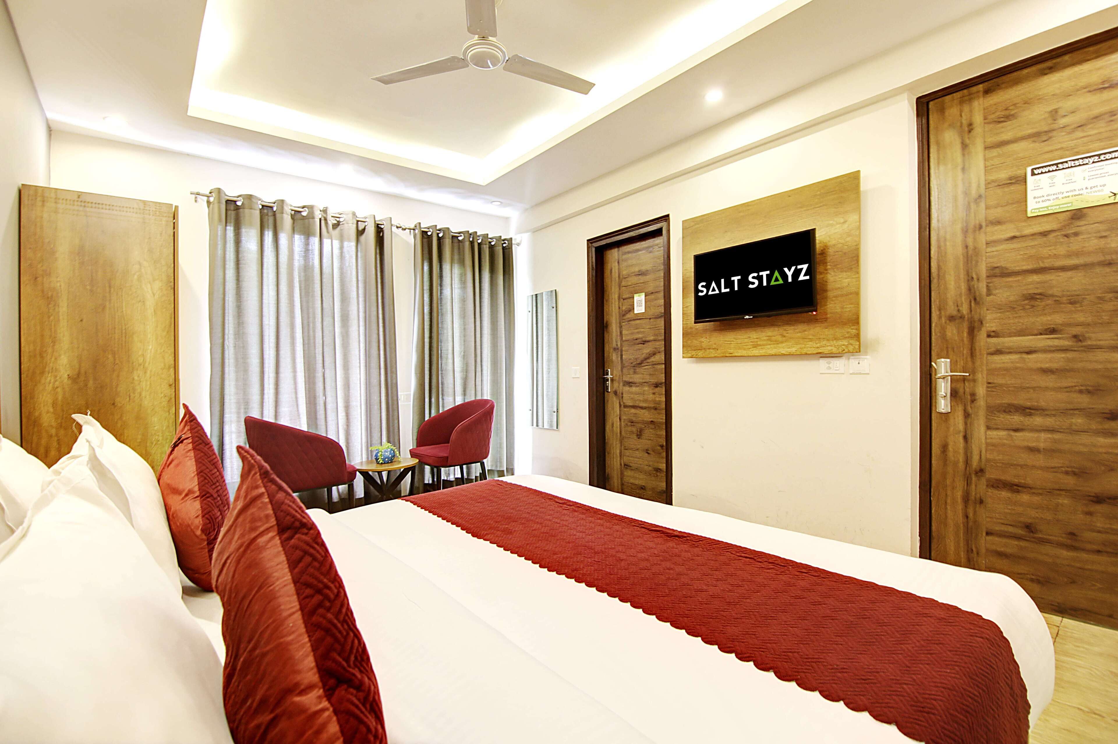 A hotel room with a bed, a desk, two chairs, a ceiling fan, and a sign on the wall.