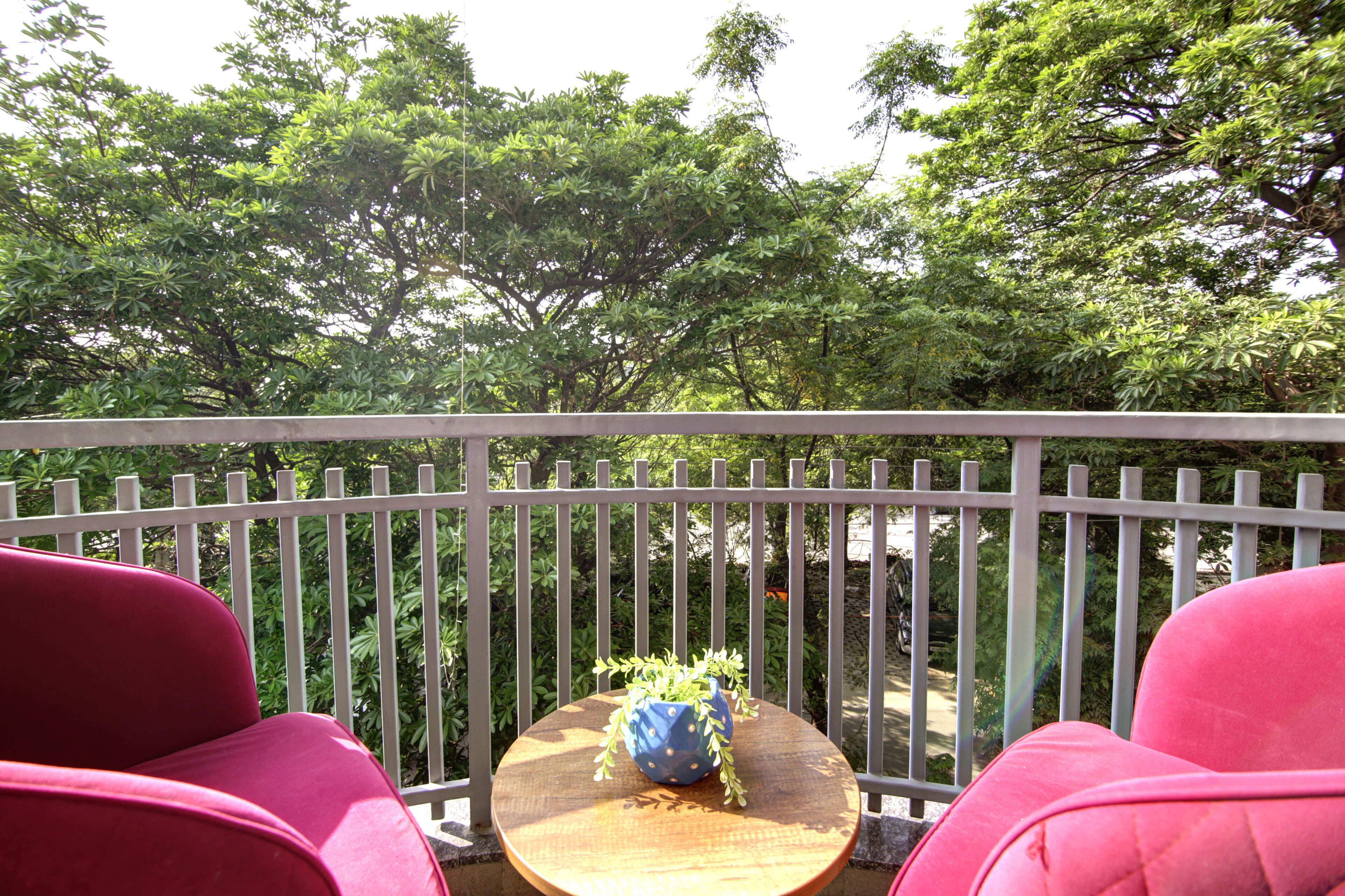 Een balkon met een ronde houten tafel, twee rode stoelen en een blauwe vaas met een plant.