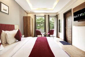 Une chambre d’hôtel avec un grand lit, un tapis rouge, deux chaises, une télévision et un balcon avec des rideaux.