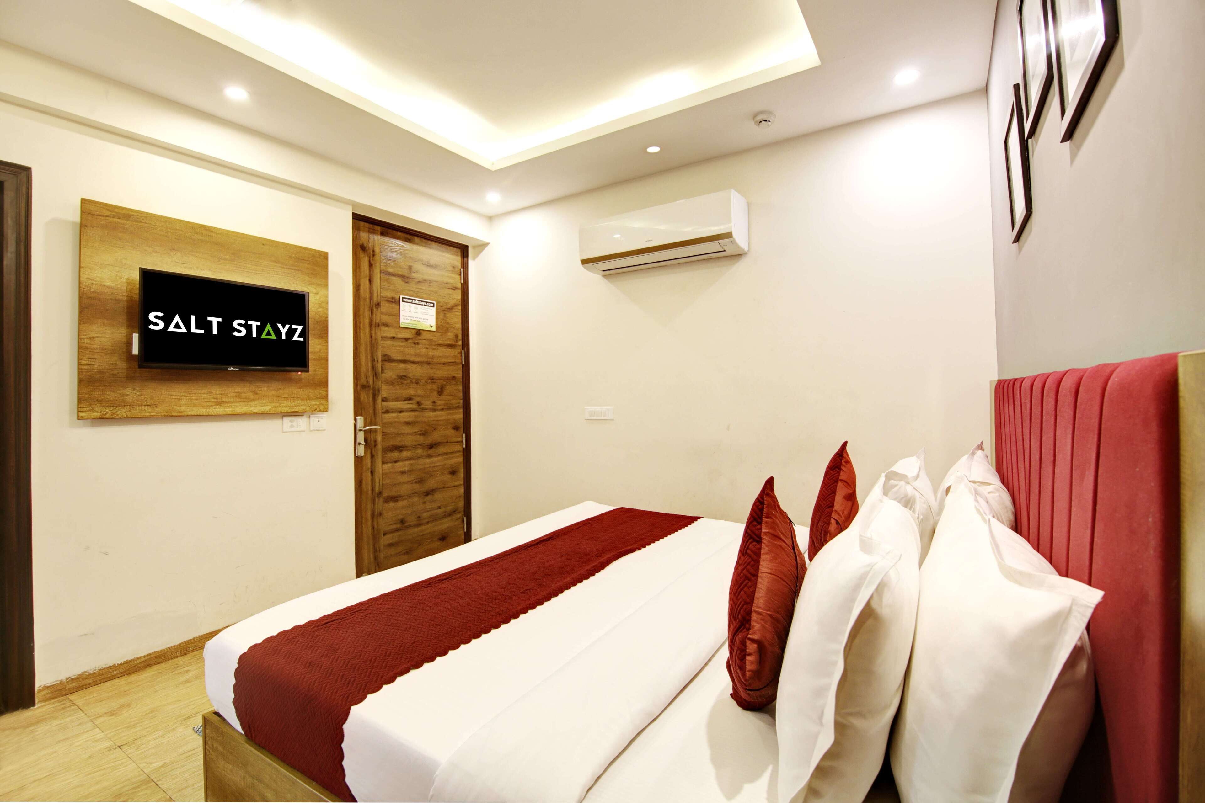 A hotel room with a bed, a TV mounted on the wall, and an air conditioning unit.