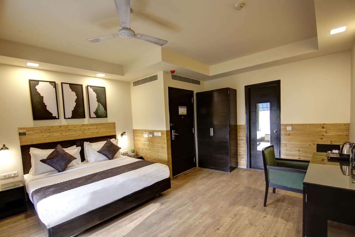 Una habitación de hotel con cama, mesitas de noche, un escritorio, una silla, un ventilador de techo y una puerta.