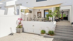 Una casa moderna con un porche cubierto, mobiliario exterior y una escalera que lleva a la entrada.