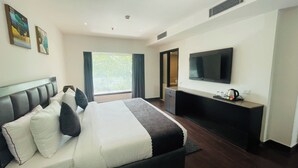Una habitación de hotel con cama, escritorio, televisor y ventana con cortinas.