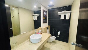 Un baño moderno con un espejo grande, un lavabo, un inodoro y una ducha. Hay toallas colgadas en la pared y un cuadro sobre el inodoro.