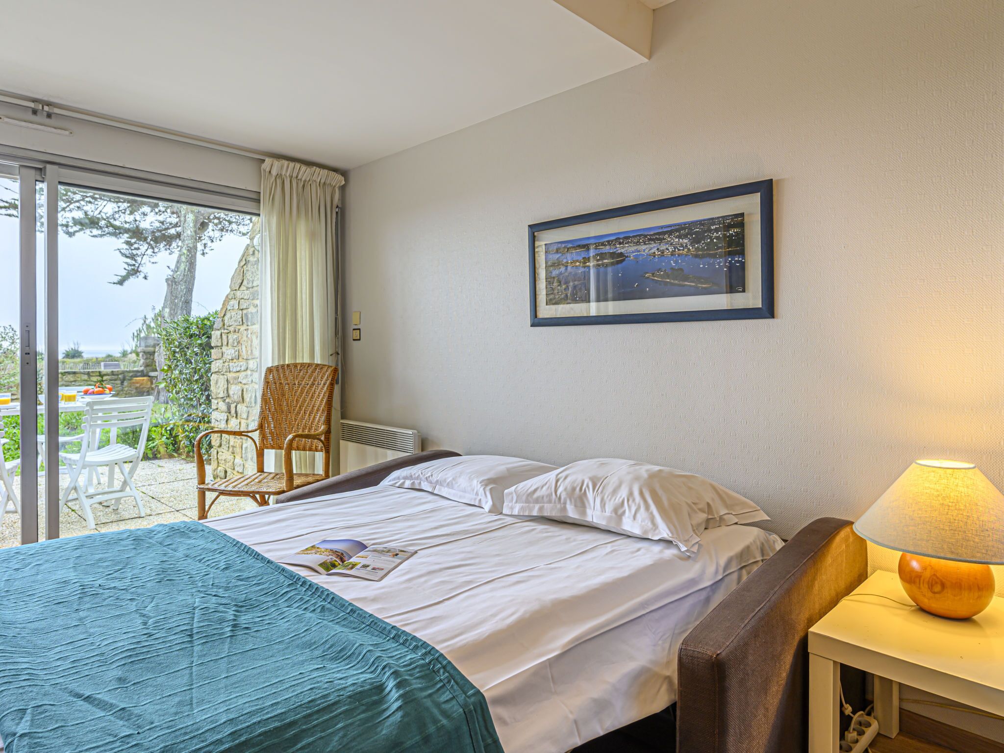 Une chambre d’hôtel avec un lit, une chaise, une table et une lampe. Il y a une fenêtre donnant sur l’extérieur.