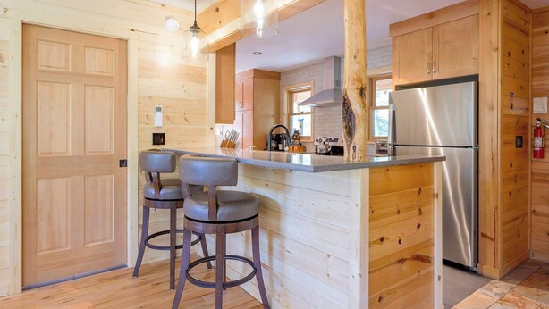 Un interno in legno con isola della cucina, sgabelli da bar, frigorifero in acciaio inossidabile e pensili in legno.